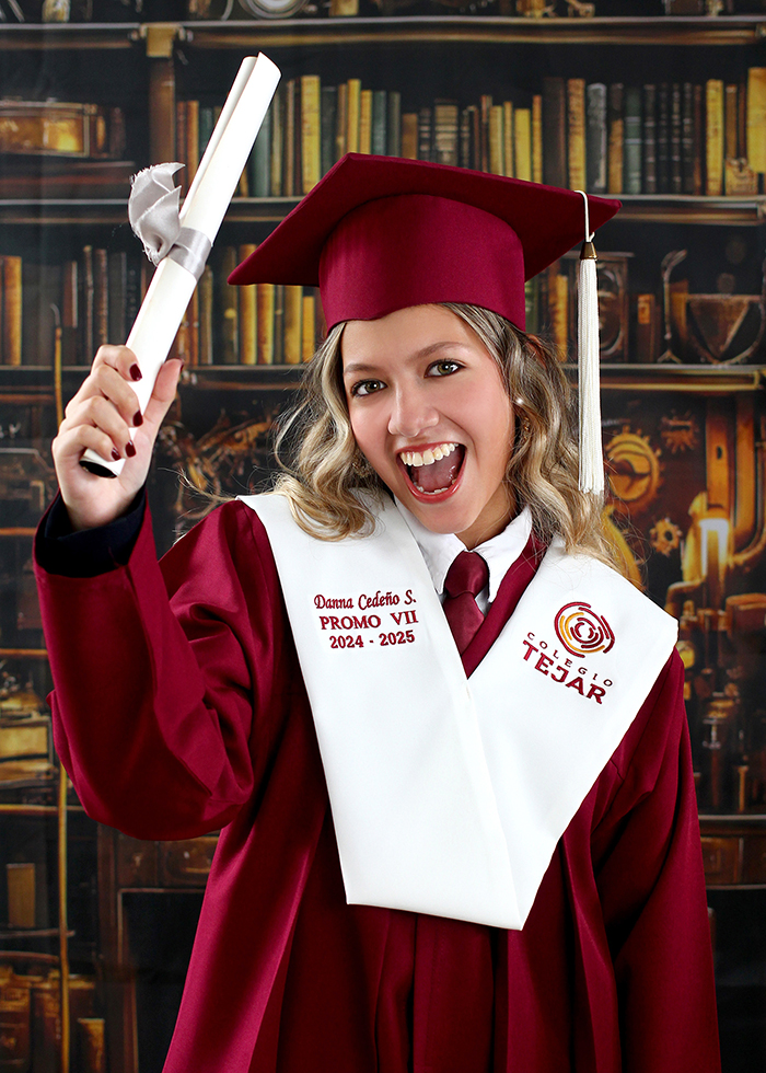 A smiling graduate holds a diploma in a maroon cap and gown with a stole reading Colegio Tejar PROMO VII 2024-2025